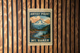 A vintage-style metal sign with a mountain landscape and a river, mounted on a wooden wall.