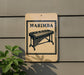 a sign with the word "MARIMBA" on it, which is a musical instrument. The sign is mounted on a wall, and there is a plant to the left of the sign.