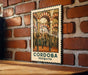 A metal sign with a decorative border and an illustration of a building, mounted on a brick wall.
