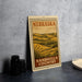 a metal sign with a vintage-style illustration of a rural landscape, including rolling hills and a field, with the text "NEBRASKA SANDHILLS COUNTRY" prominently displayed.