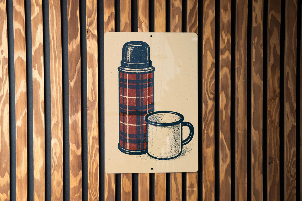 A metal sign with a plaid pattern and a white mug is displayed against a wooden wall.