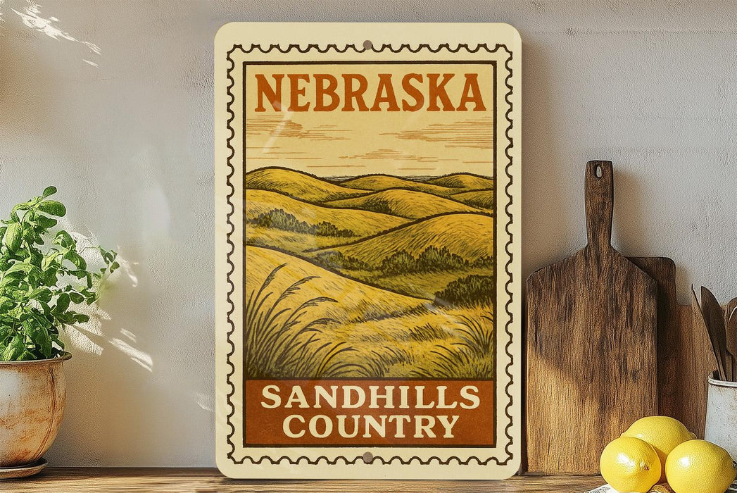 a vintage-style metal sign with the text "NEBRASKA SANDHILLS COUNTRY" displayed prominently. The sign is mounted on a wall, and there are some kitchen utensils, such as a wooden cutting board and a knife, as well as a potted plant and a bowl of fruit, including lemons, in the background.