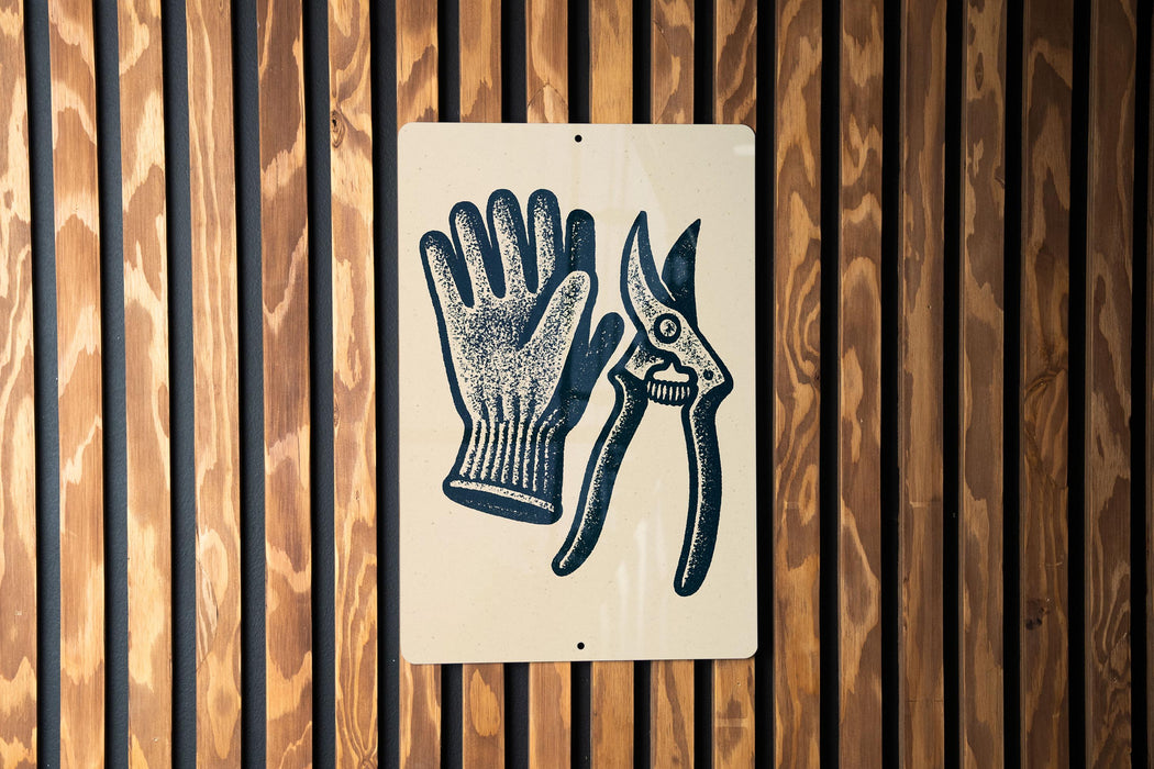 A sign with a pair of gardening gloves and pruning shears is displayed on a wooden wall.