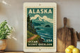 A vintage-style postage stamp depicting a scenic overlook in Alaska, USA, with mountains, trees, and a body of water.