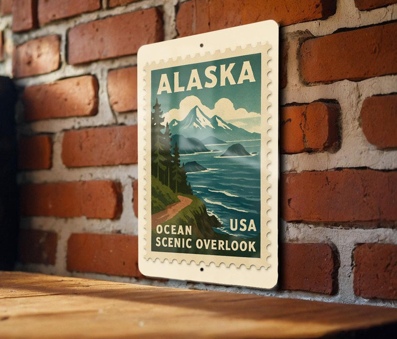 A vintage-style postage stamp depicting Alaska, with a mountain landscape and ocean scene, is displayed on a brick wall.