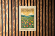A framed poster of a field of flowers hangs on a wooden wall.