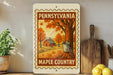 A framed poster of a maple syrup production scene from Pennsylvania, featuring a tree, a house, and a bucket, is displayed on a shelf next to a wooden cutting board and a potted plant.