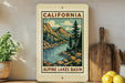 A framed vintage-style illustration of the Alpine Lakes basin in California, featuring a mountain landscape with pine trees and a river.