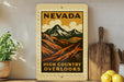 A framed poster of a mountain landscape with the text "NEVADA HIGH COUNTRY OVERLOOKS" is displayed on a shelf next to a wooden cutting board and a potted plant.