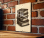 A sign with a stack of books on it is hanging on a brick wall.
