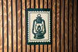 A lantern-like object is displayed on a wooden wall, with a green and white border around it.