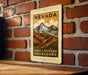 A vintage-style sign for Nevada, featuring a mountain landscape with clouds, mounted on a brick wall.