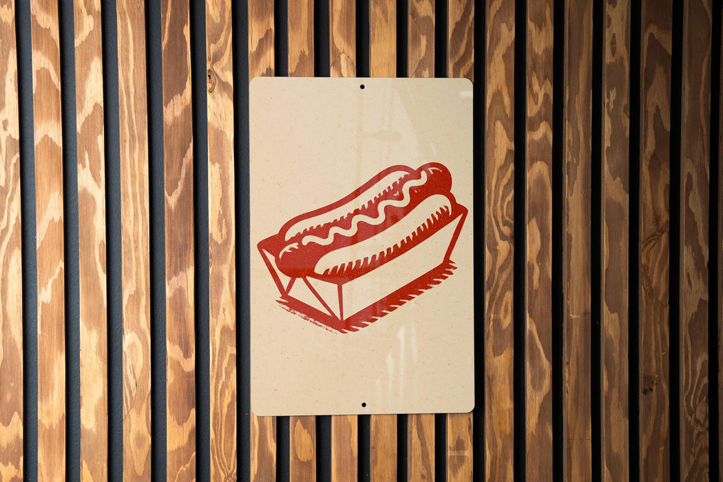 A sign with a red hot dog in a basket is displayed on a wooden wall.