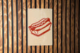 A sign with a red hot dog in a basket is displayed on a wooden wall.