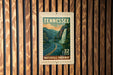A Tennessee postage stamp featuring a scenic waterfall and road, mounted on a wooden wall.