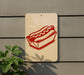 a sign with a red hot dog on a bun, mounted on a wall.