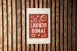 A sign with the text "Laundromat Romat" is displayed on a wooden wall.