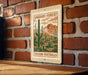 A wooden table with a framed poster of a desert landscape featuring cacti and mountains, mounted on a brick wall.