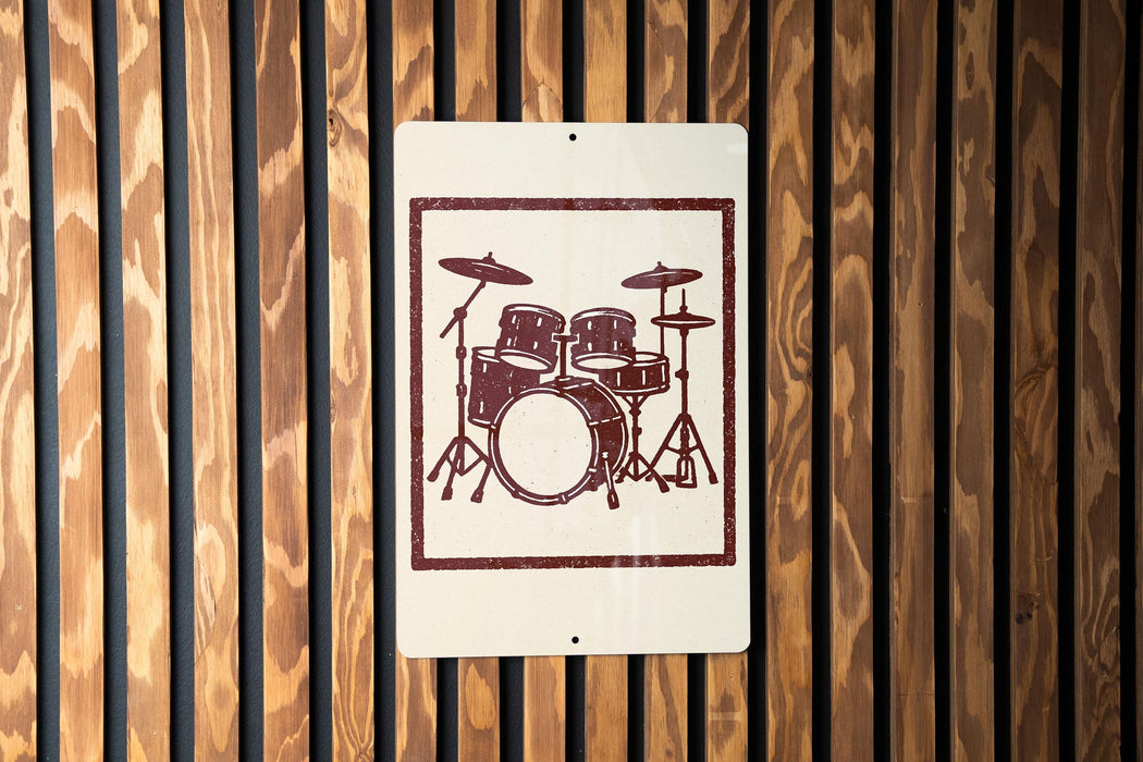a sign with a drum set on it, mounted on a wooden wall.