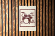 a sign with a drum set on it, mounted on a wooden wall.