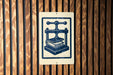a sign with a blue and white design depicting a book press, mounted on a wooden wall.