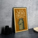 A framed illustration of a green metal milk can with flowers on a yellow background, placed on a dark surface next to some black camera lenses.