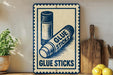 A vintage-style sign advertising glue sticks is displayed on a wooden shelf, with a potted plant and a wooden cutting board nearby.