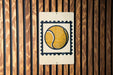 A tennis ball painted on a white sign with a black border, mounted on a wooden wall.