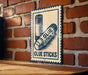 A sign on a brick wall that reads "GLUE STICKS" and features an illustration of two glue sticks.