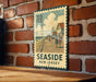 A vintage-style metal sign with a beach scene and people on a boardwalk, mounted on a brick wall.