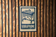 A metal sign with a graphic of a musical instrument, specifically a vibraphone, mounted on a wooden wall.