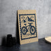 a wooden sign with a bicycle illustration on it, placed on a table next to some black camera lenses.