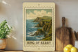 A framed print of a coastal landscape with cliffs and the ocean is displayed on a shelf, accompanied by kitchen utensils and a potted plant.