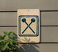a sign with a symbol of two crossed drumsticks on a beige background, mounted on a wall.