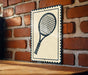A black and white tennis racket is mounted on a brick wall, with a wooden table below it.
