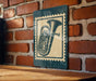 A metal sign with a vintage-style illustration of a tuba is mounted on a brick wall.