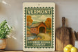 a vintage-style sign for Vermont's Covered Bridge Country, with a wooden bridge and autumn trees depicted on the sign.