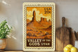A framed vintage-style illustration of the Valley of the Gods in Utah, featuring a desert landscape with mountains and rock formations.