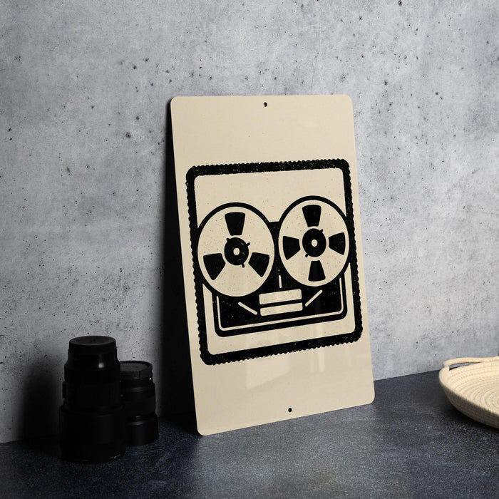 a sign with a stylized graphic of a tape recorder or record player, along with some black and white objects, such as a stack of black camera lenses and a beige woven basket.
