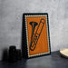 a framed illustration of a trombone on a wall, with a stack of black camera lenses placed next to it.