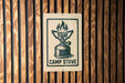 A sign with a graphic of a camp stove is mounted on a wooden wall.