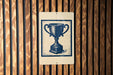 A blue and white sign with a trophy icon is mounted on a wooden wall.