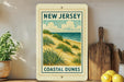 A framed poster of a coastal dune landscape hangs on a wall, with a wooden cutting board and a potted plant to the side.