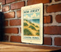 A metal sign with a coastal dune landscape and the text "NEW JERSEY COASTAL DUNES" is displayed on a brick wall.