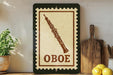 a framed stamp-like sign with the word "OBOE" on it, placed on a wooden surface next to a potted plant and a wooden cutting board.