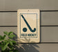a sign that reads "FIELD HOCKEY" with a hockey stick symbol on it, mounted on a wall.