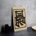 a wooden chair with a woven seat and legs, placed on a gray countertop next to a stack of black camera lenses.