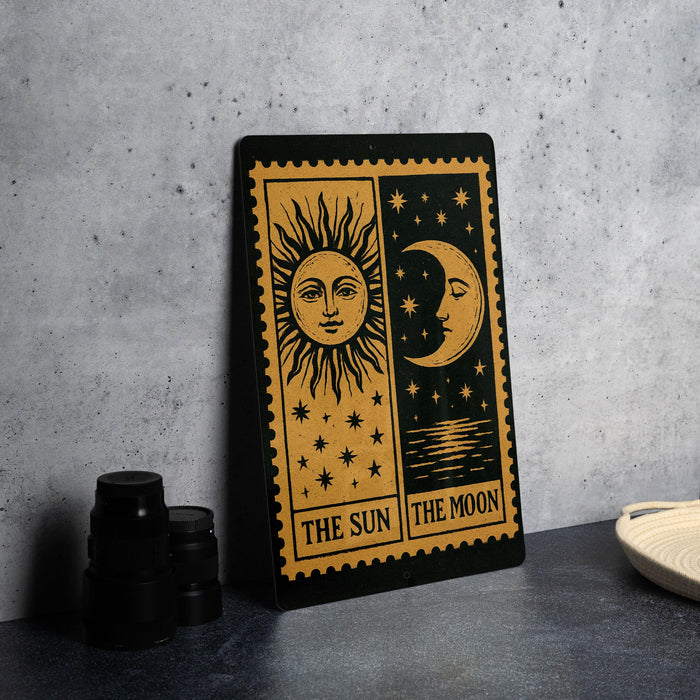 a black and gold sign with the words "THE SUN THE MOON" printed on it, standing on a gray countertop next to some black camera lenses.