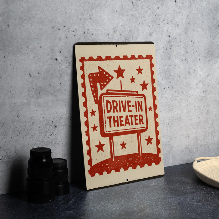 A sign that reads "DRIVE-IN THEATER" is displayed on a table, with a stack of black camera lenses and a white dish visible to the side.