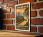 A vintage-style postage stamp from Arkansas depicting a scenic road leading to a canyon, mounted on a brick wall.